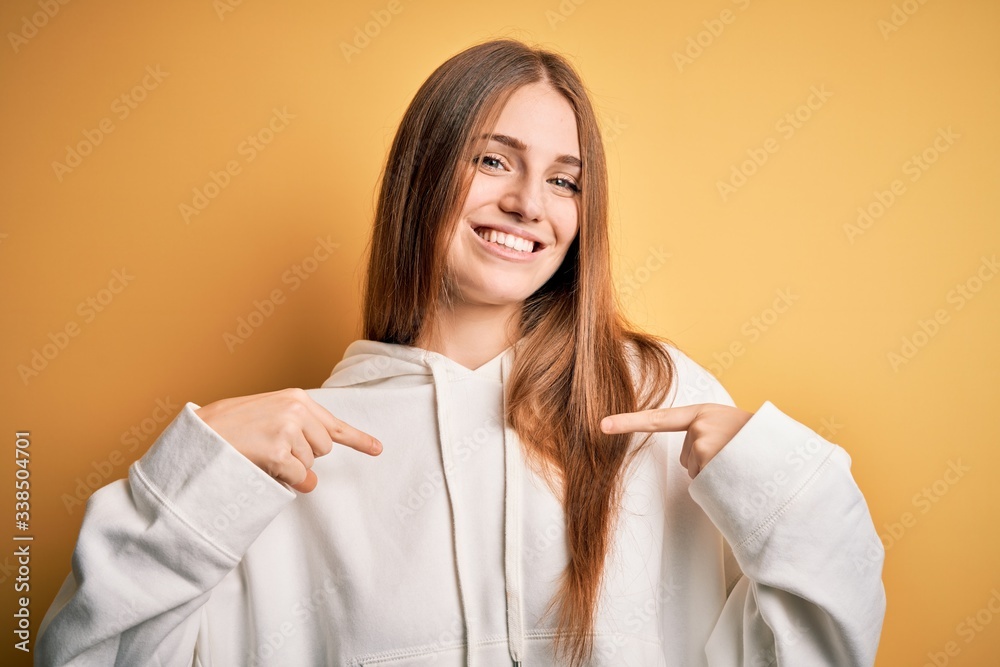 Young beautiful redhead sporty woman wearing sweatshirt over isolated yellow background looking confident with smile on face, pointing oneself with fingers proud and happy. Young beautiful redhead sporty woman wearing sweatshirt over isolated yellow background looking confident with smile on face, pointing oneself with fingers proud and happy.