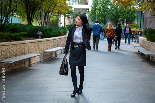 Beautiful Chinese Asian woman in fashionable business attire is enjoying a nice day walking around downtown Chicago in the afternoon. She carries a trendy handbag and black blazer with red lipstick
