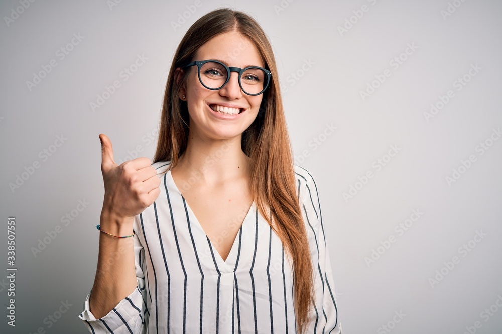 Young beautiful redhead woman wearing casual striped t-shirt and glasses doing happy thumbs up gesture with hand. Approving expression looking at the camera showing success. Young beautiful redhead woman wearing casual striped t-shirt and glasses doing happy thumbs up gesture with hand. Approving expression looking at the camera showing success.