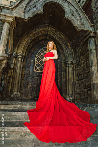 A woman in a red dress stands on a background of a medieval castle