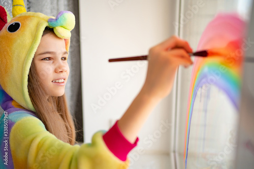 teen girl in kigurumi draws rainbow on window home photo