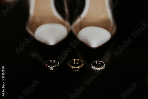 Wedding accessories on a black background. Wedding rings, white bride's shoes.