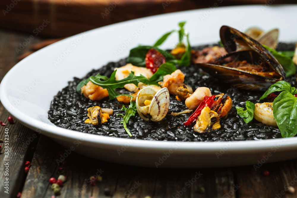 Closeup view on italian cuisine dish black risotto with seafood on the white plate on the dark wooden table, horizontal format