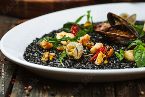 Closeup view on italian cuisine dish black risotto with seafood on the white plate on the dark wooden table  horizontal format