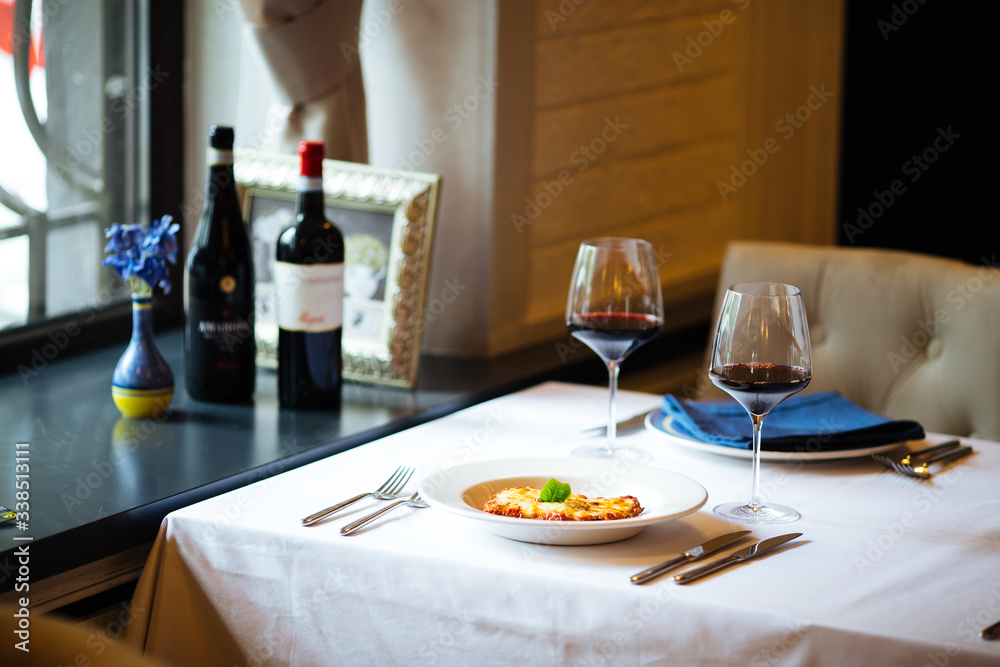 Appetizing fresh cooked italian cuisine dish lasagna with a glass of red wine on the white plate on the white served table, horizontal format Appetizing fresh cooked italian cuisine dish lasagna with a glass of red wine on the white plate on the white served table, horizontal format
