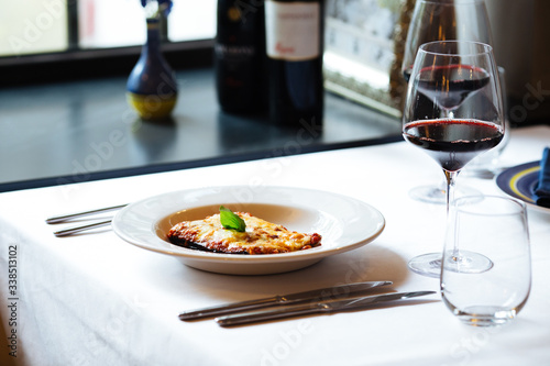 Appetizing fresh cooked italian cuisine dish lasagna with a glass of red wine on the white plate on the white table  horizontal format