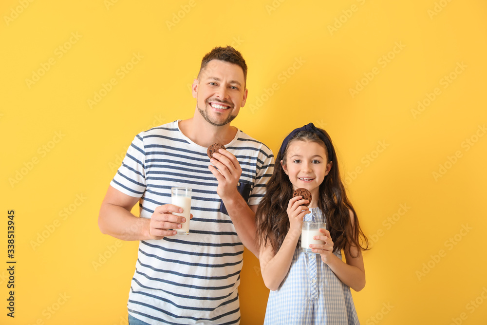 Father and daughter drinking milk with cookies on color background Father and daughter drinking milk with cookies on color background