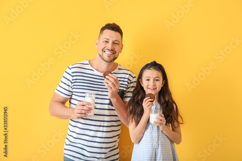 Father and daughter drinking milk with cookies on color background
