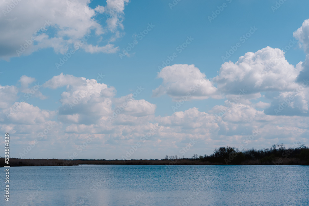 Beautiful spring cloudy sky, panorama, landscape. The lake and the snow-white clouds reflected in it. Haze in the blue sky and a beautiful blue river