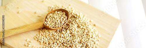 barley groats with a wooden spoon on a white wooden background