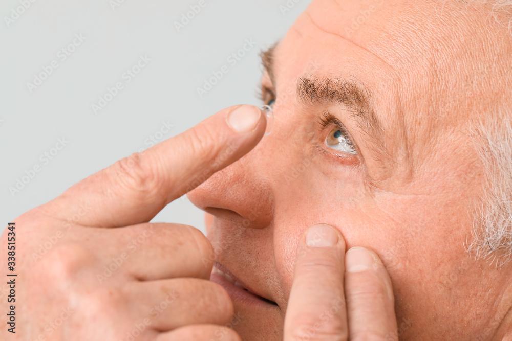 Obraz premium Mature man putting in contact lenses against light background