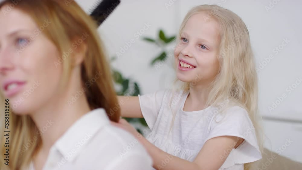 Slowmo of adorable blond girl with toothy smile brushing her mothers hair Slowmo of adorable blond girl with toothy smile brushing her mothers hair