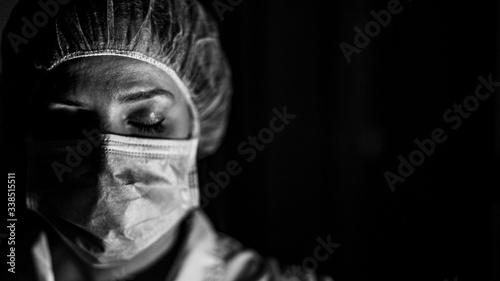 Portrait black and white of young female surgeon, wearing mask and a surgical mask, in front of black background