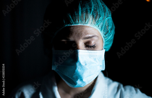 Portrait of young female surgeon, wearing mask and a surgical mask, in front of black background