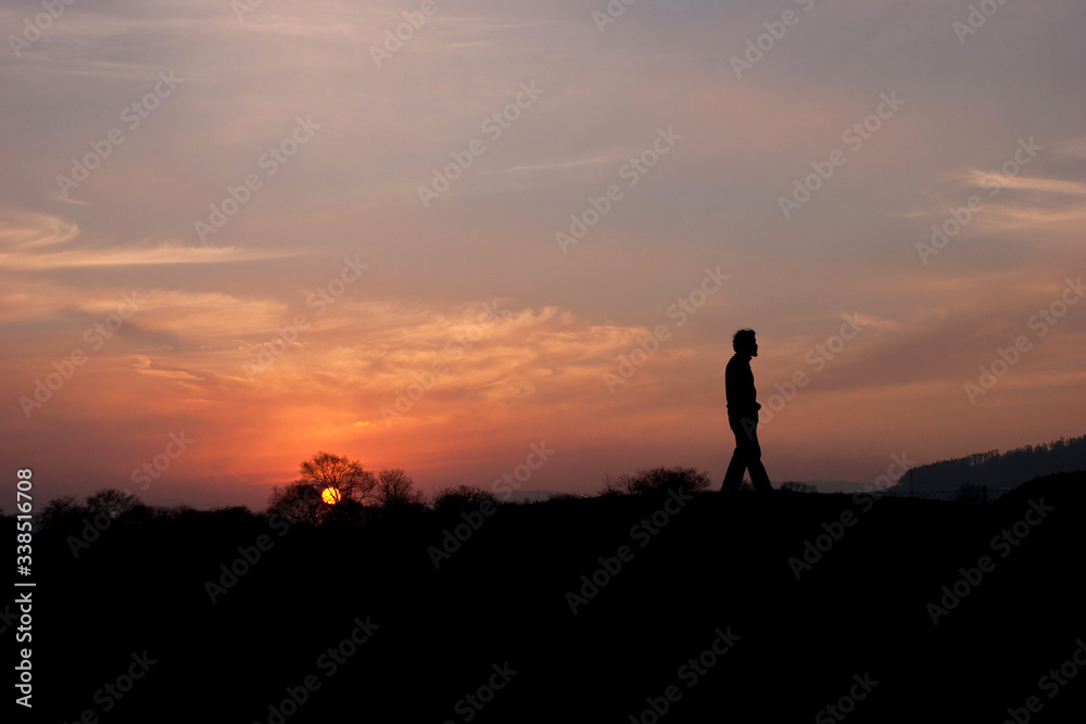 man walks alone in landscape at sunset backlit