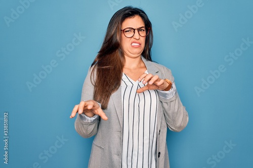 Young hispanic business woman wearing glasses standing over blue isolated background disgusted expression, displeased and fearful doing disgust face because aversion reaction.