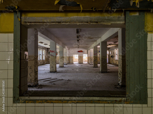 Looking through the interior window of an abandoned cafeteria, with trash on the floor in a derelict building