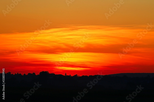 Sunset on the background of the field, the silhouette of the village. © Dzmitry