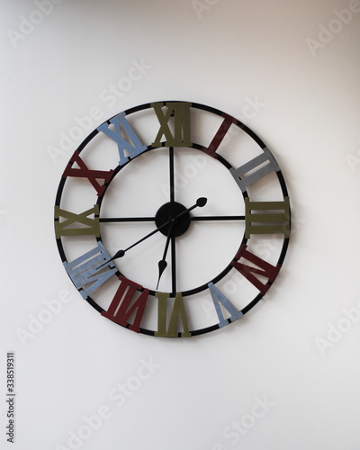 Reloj de gran tamaño con los números romanos de diferentes colores colgado en la pared. 