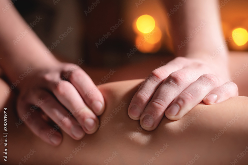 Close-up of the hands of a professional massage therapist men doing wellness massage shins and legs for a client to a girl in a professional massage salon on the background of burning candles