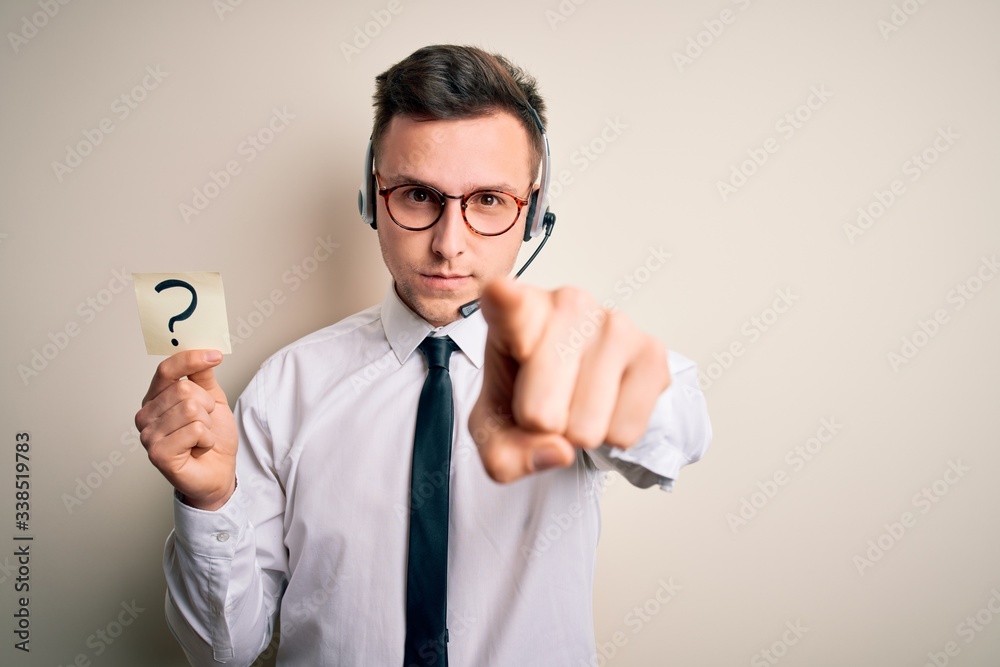 Young call center operator man wearing headset holding paper note with question mark pointing with finger to the camera and to you, hand sign, positive and confident gesture from the front Young call center operator man wearing headset holding paper note with question mark pointing with finger to the camera and to you, hand sign, positive and confident gesture from the front