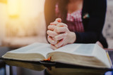 Close up of woman's hands praying on open bible while sitting on the sofa at home