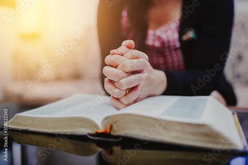 Close up of woman's hands praying on open bible while sitting on the sofa at home