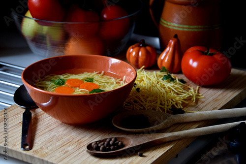 delicate chicken broth in a bowl next to tomatoes, spices and kitchen utensils