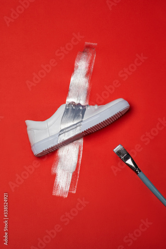 White sport sneaker shoe painted with a silver paint with brush shot from above on red background photo