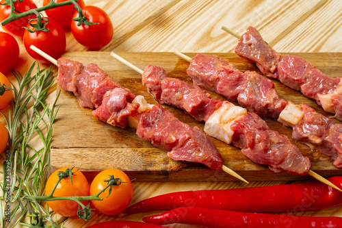Raw kebab from meat on a wooden background with vegetables.