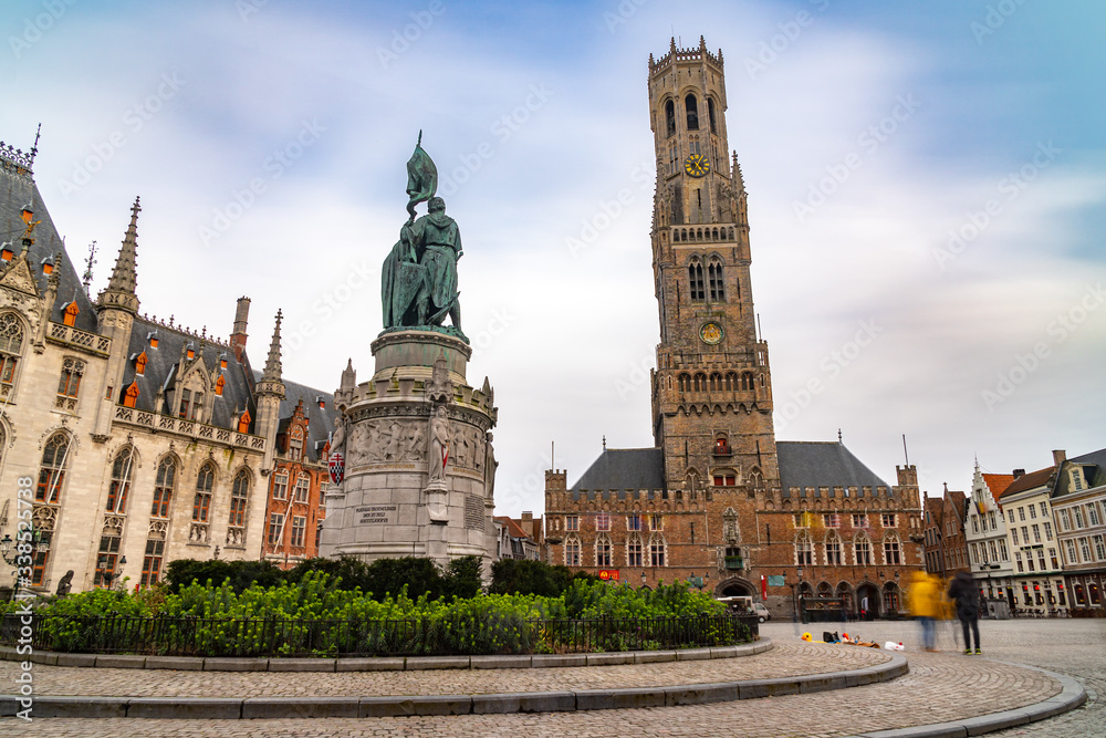 Obraz premium Looking up at Belfry of Bruges, medieval bell tower the city of UNESCO world heritage, during winter time in a blue sky background, old style lamp post in background., long exposure.