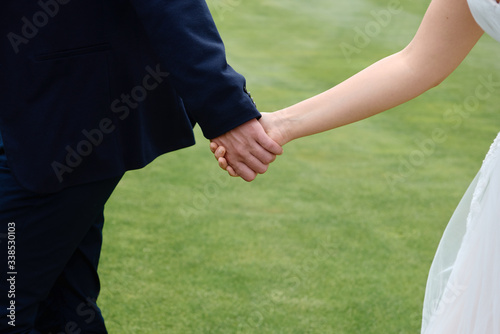 Bride and groom holding hands and walking on green grass of golf course, copy space. Happy wedding couple