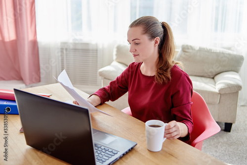 Portrait of young confident business woman sitting at wood desk, drinking coffee and reading documents at home office, copy space