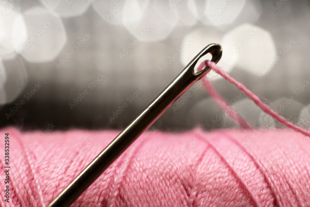 A macro image of a needle s eye threaded, pink thread