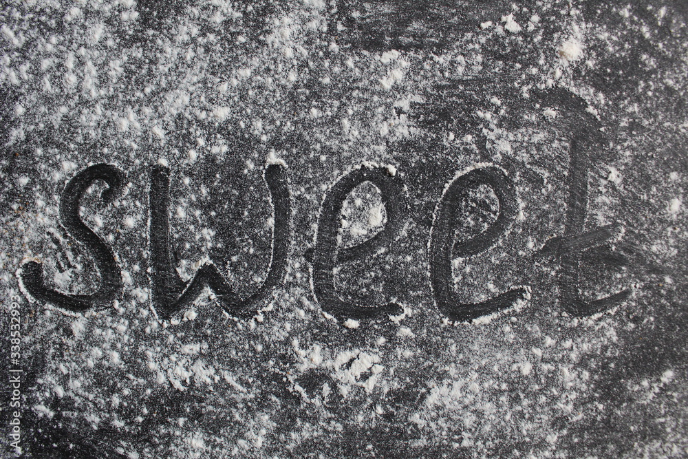 inscriptions the word sweet is written on a gray stone black dark background black and white sprinkled with powdered sugar or flour there are cups mugs red green blue with tea coffee inscriptions the word sweet is written on a gray stone black dark background black and white sprinkled with powdered sugar or flour there are cups mugs red green blue with tea coffee