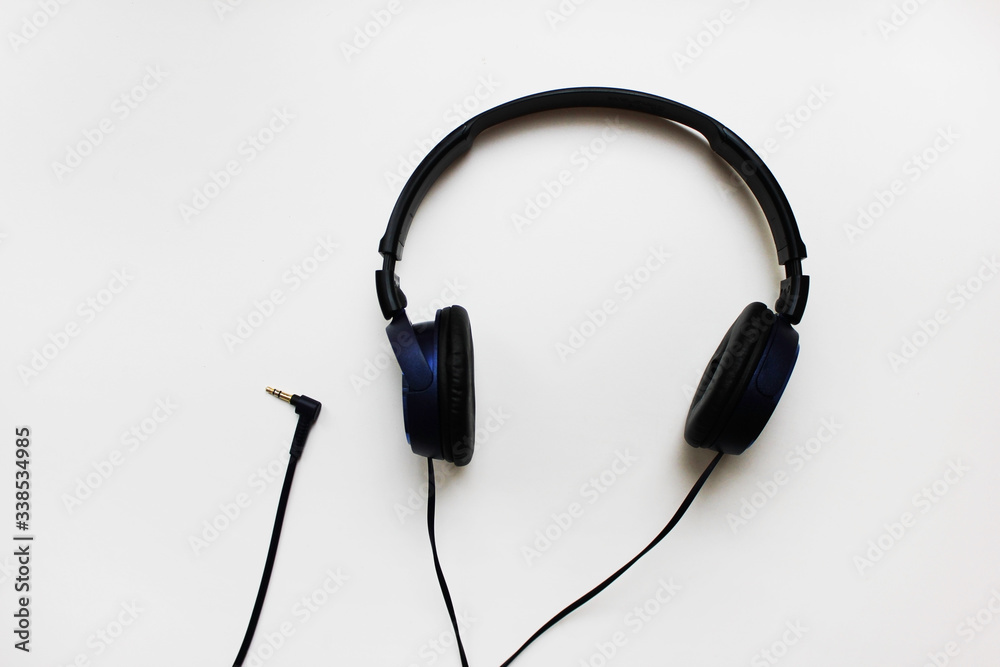 Wired headphones with cord isolated on white table background. Old black on-ear headphones close up view, music listening technology device top view Wired headphones with cord isolated on white table background. Old black on-ear headphones close up view, music listening technology device top view