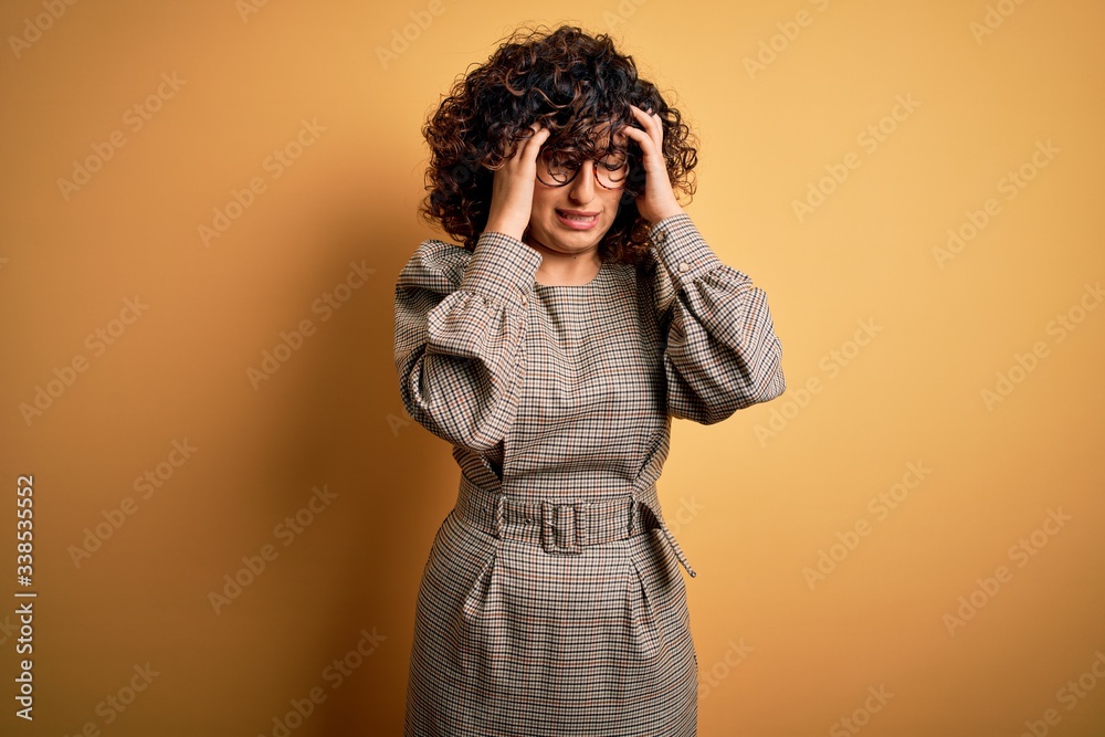 Beautiful arab business woman wearing dress and glasses standing over yellow background with hand on headache because stress. Suffering migraine. Beautiful arab business woman wearing dress and glasses standing over yellow background with hand on headache because stress. Suffering migraine.