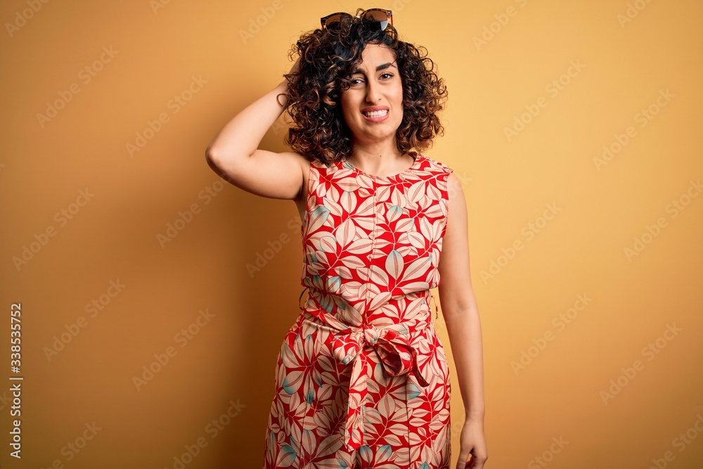 Young beautiful curly arab woman on vacation wearing summer floral dress and sunglasses confuse and wonder about question. Uncertain with doubt, thinking with hand on head. Pensive concept. Young beautiful curly arab woman on vacation wearing summer floral dress and sunglasses confuse and wonder about question. Uncertain with doubt, thinking with hand on head. Pensive concept.