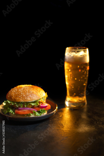 Fresh hamburger with steak, lettuce on the background of a blurred glass of light beer on a black background.