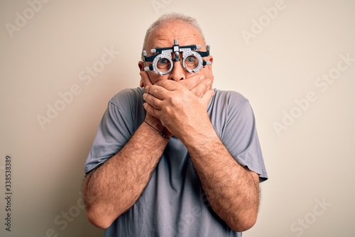 Middle age hoary man controlling vision wearing optometry glasses over white background shocked covering mouth with hands for mistake. Secret concept.