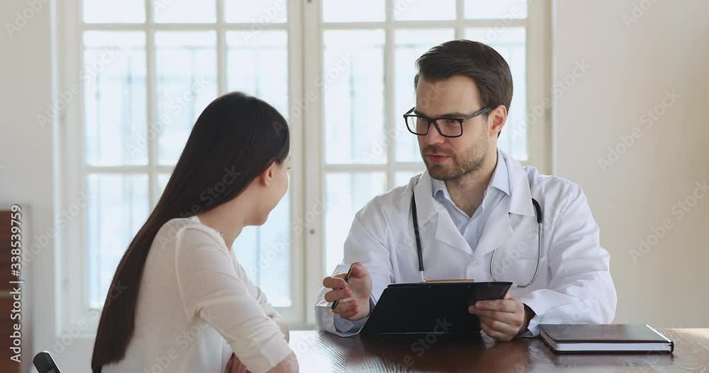 Qualified male doctor in white suit holding clipboard, listening to female patient, filling medical history at check up meeting. Professional therapist physician explaining treatment at clinic visit. Qualified male doctor in white suit holding clipboard, listening to female patient, filling medical history at check up meeting. Professional therapist physician explaining treatment at clinic visit.