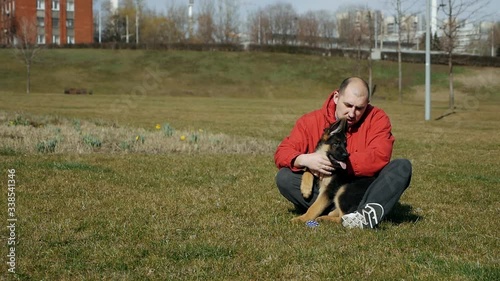 A man sits on the grass and hugs his German shepherd puppy dog on a grassy lawn. Slow motion photo