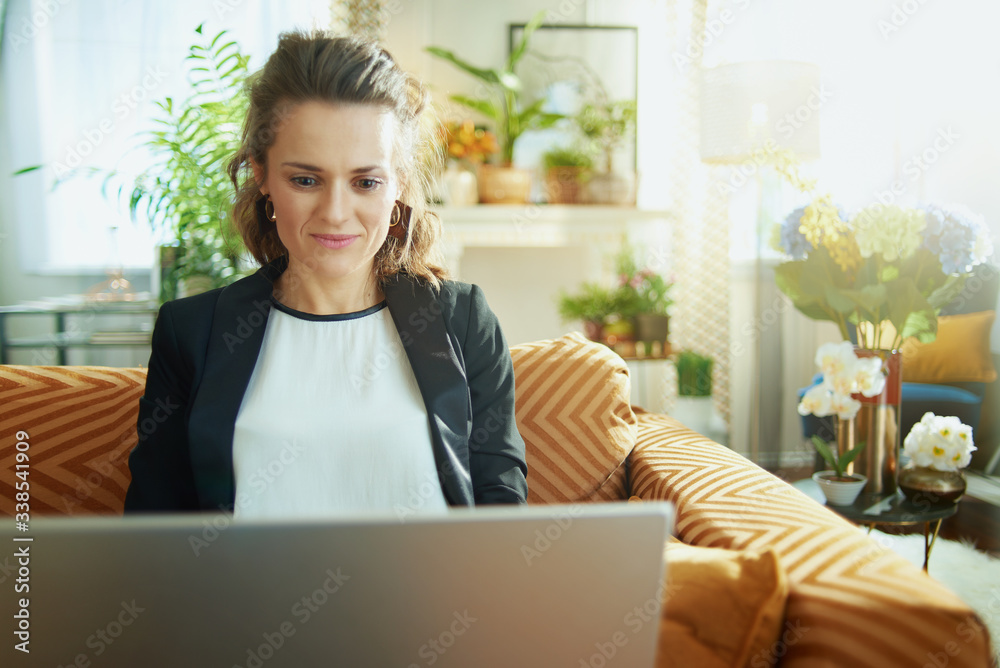 trendy housewife writing on laptop while sitting on sofa trendy housewife writing on laptop while sitting on sofa