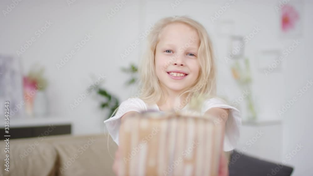 Portrait shot of adorable little girl with blond hair smiling and showing present to camera Portrait shot of adorable little girl with blond hair smiling and showing present to camera