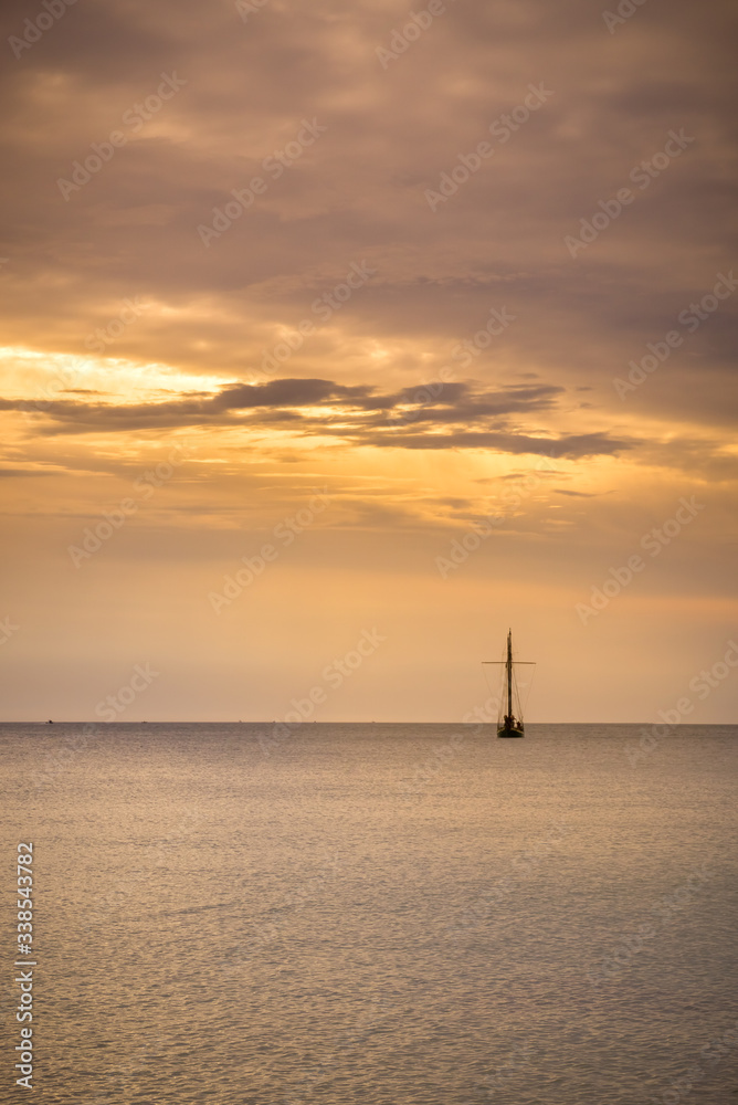 isolated boat at sunset. sky is cloudy and orange. peaceful mood. portrait format