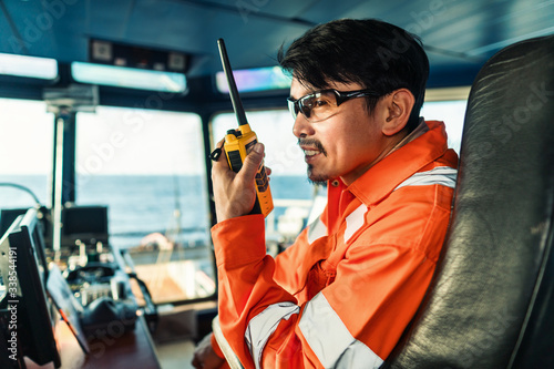 Filipino deck Officer on bridge of vessel or ship wearing coverall during navigaton watch sea . He is speaking on portable GMDSS VHF radio, short range communication Stock-foto | Adobe Stock