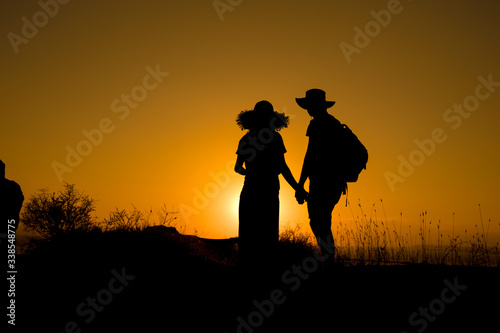Silhouettes of two hikers with backpacks enjoying sunset view from top of a mountain. Travel concept