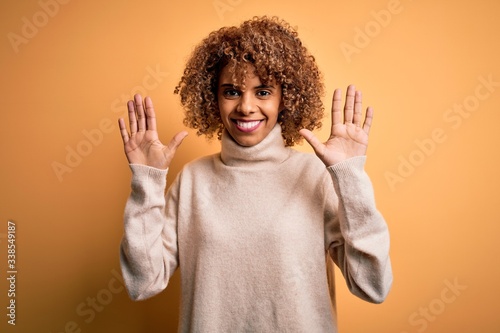 Young beautiful african american woman wearing turtleneck sweater over yellow background showing and pointing up with fingers number ten while smiling confident and happy.