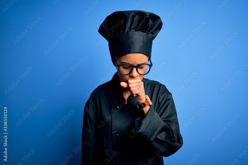 Young african american chef woman wearing cooker uniform and hat over blue background feeling unwell and coughing as symptom for cold or bronchitis. Health care concept.