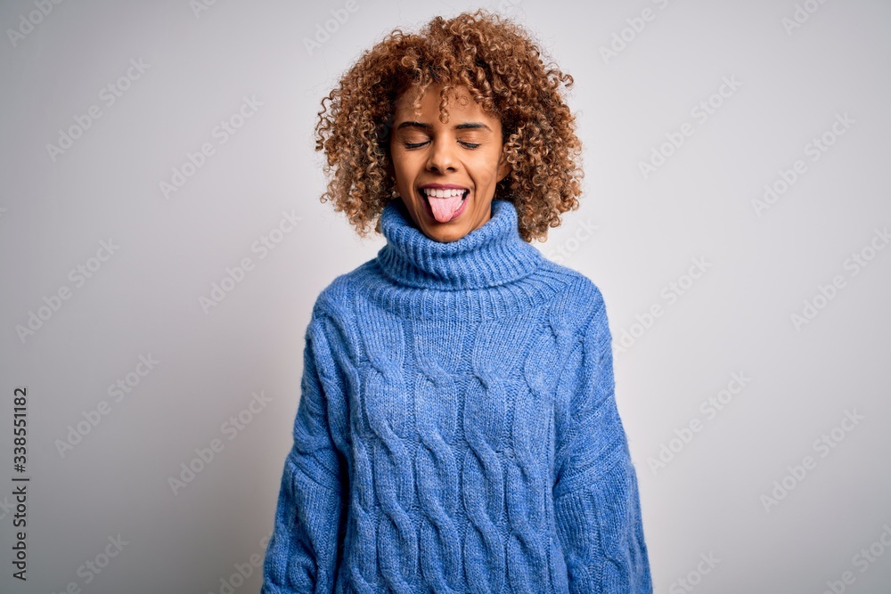 Young beautiful african american woman wearing turtleneck sweater over white background sticking tongue out happy with funny expression. Emotion concept. Young beautiful african american woman wearing turtleneck sweater over white background sticking tongue out happy with funny expression. Emotion concept.